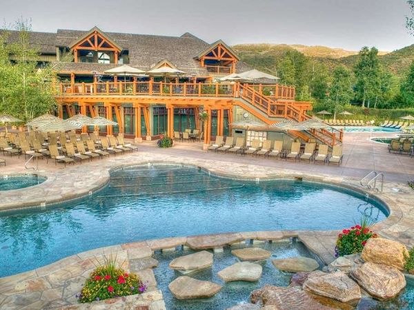 The image shows a luxurious outdoor pool area in front of a large building with wooden architecture, surrounded by hills and greenery, ending the sentence.