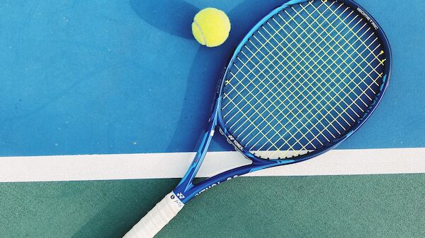 A tennis racket and a tennis ball are placed on a blue and green court, with the racket touching the boundary line.