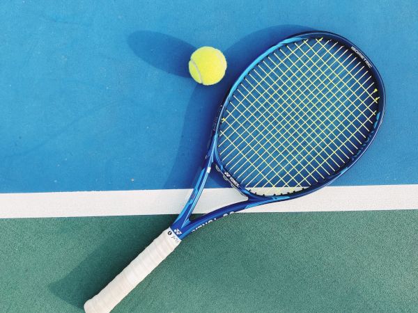 A tennis racket and a tennis ball are placed on a blue and green court, with the racket touching the boundary line.
