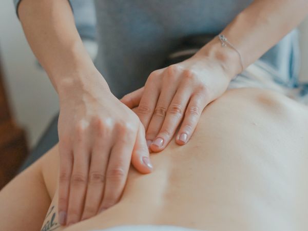 A person is giving a back massage to someone lying face down on a bed or massage table, applying pressure with both hands on the person's back.