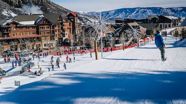 A bustling ski resort with people skiing and snowboarding, charming lodges, and mountainous surroundings under a clear blue sky.