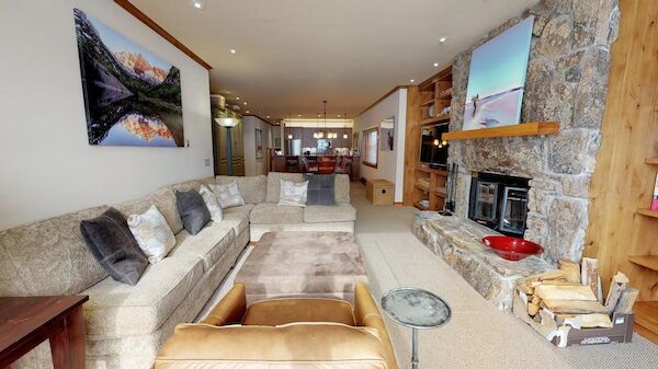 The image shows a cozy living room with a large sofa, a stone fireplace, and artwork on the walls. It has a warm, inviting ambiance.