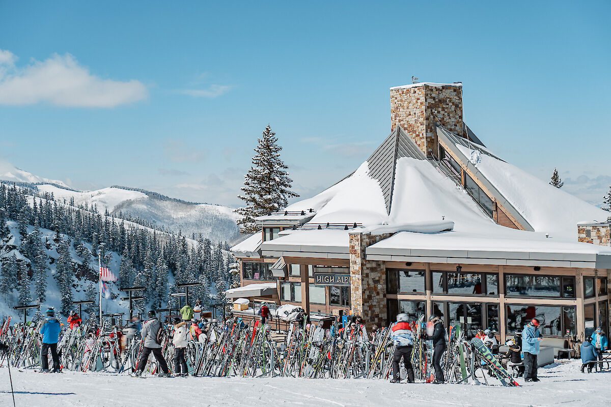 A snowy ski resort scene with people and skis outside a cozy lodge under a clear blue sky. Perfect winter getaway vibes.