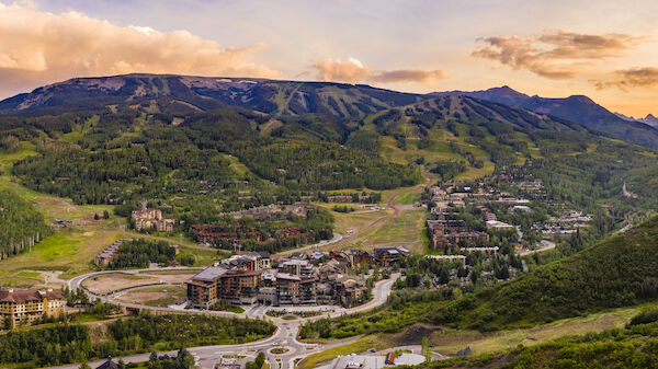A scenic view of a mountainous area with ski slopes, resorts, and lush green vegetation under a cloudy sky at sunset.